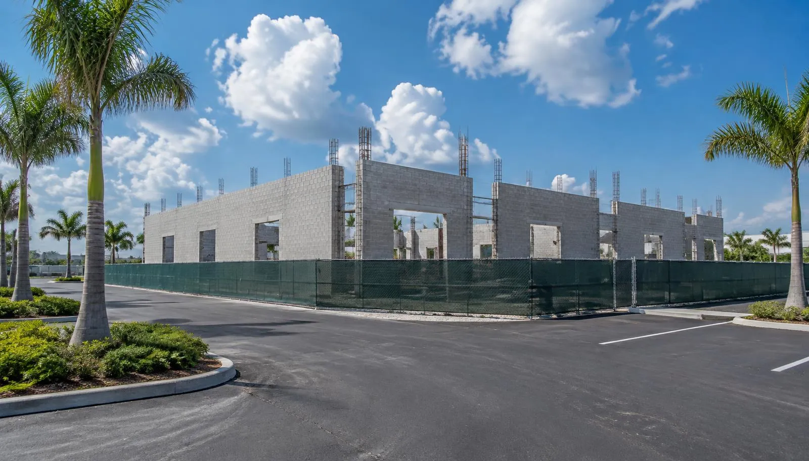 A South Florida commercial construction site featuring a partially built cinder block warehouse structure surrounded by construction fencing and a paved lot.
