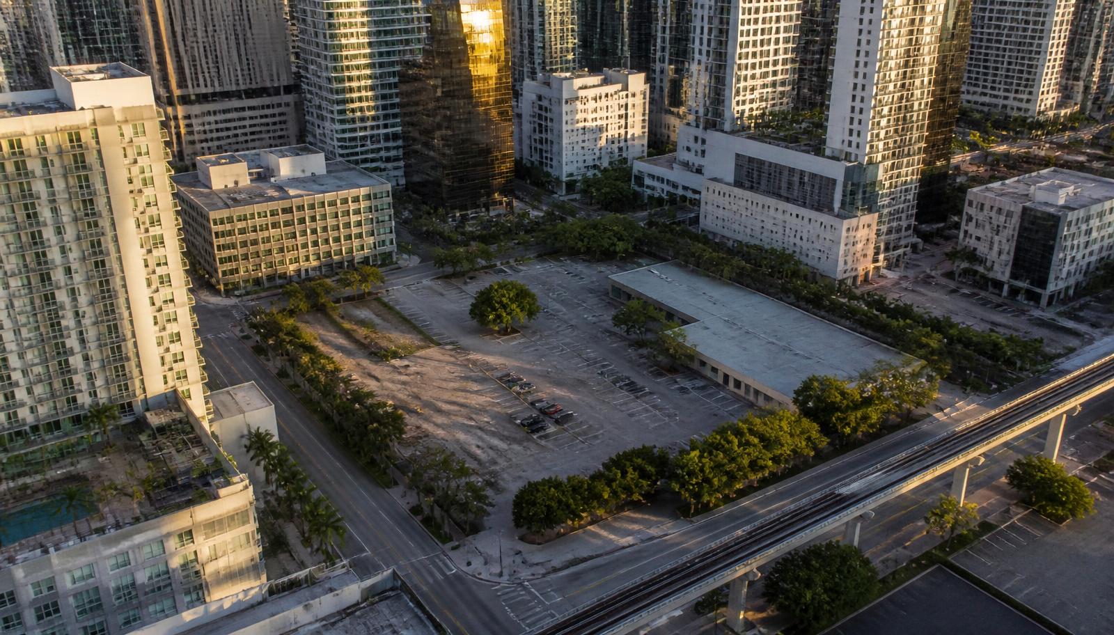 An aerial view of an urban surface commercial parking lot and covered land parcel in downtown Miami, South Florida, surrounded by commercial buildings.