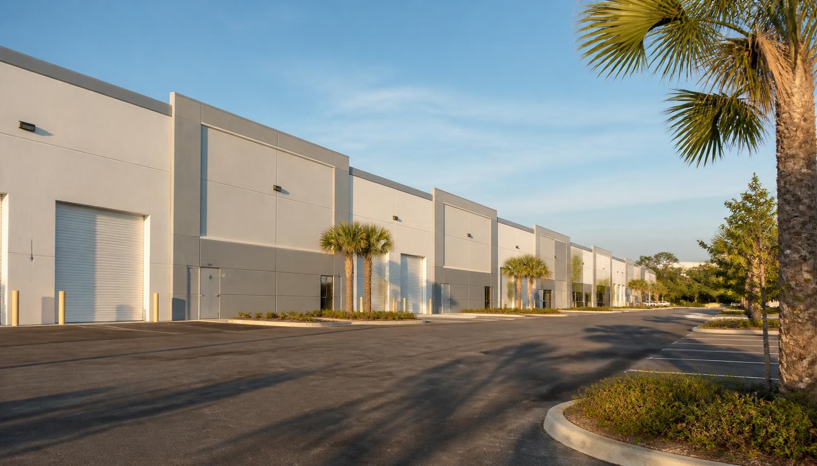 An exterior view of a multi-tenant industrial flex space and warehouse facility in Fort Myers, Florida, featuring grade-level roll-up doors and clear drive aisles.
